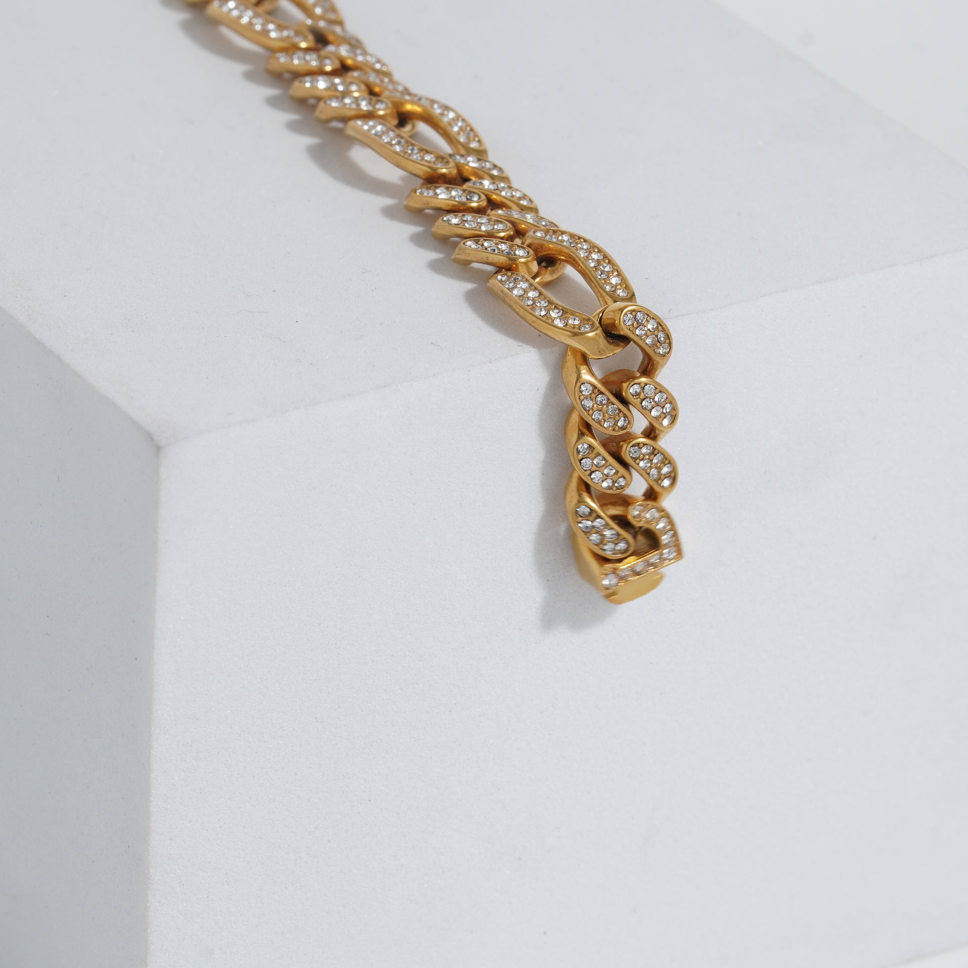 Gold chain bracelet with embedded stones on a light gray background