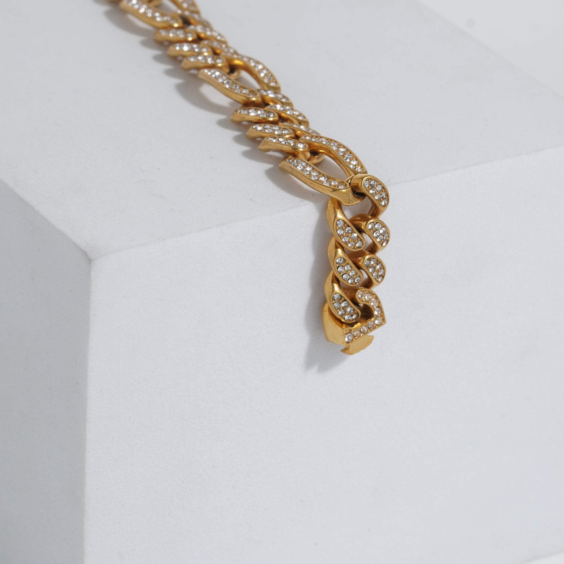 Gold chain bracelet with embedded stones on a light gray background